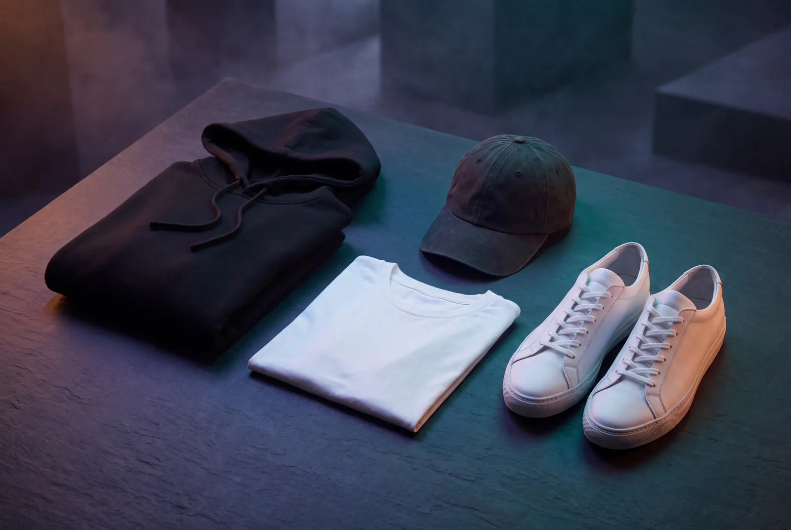 Streetwear flat lay with a black hoodie, white tee, cap and white sneakers